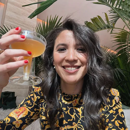 Amy smiling and holding up a mimosa in front of palm leaves